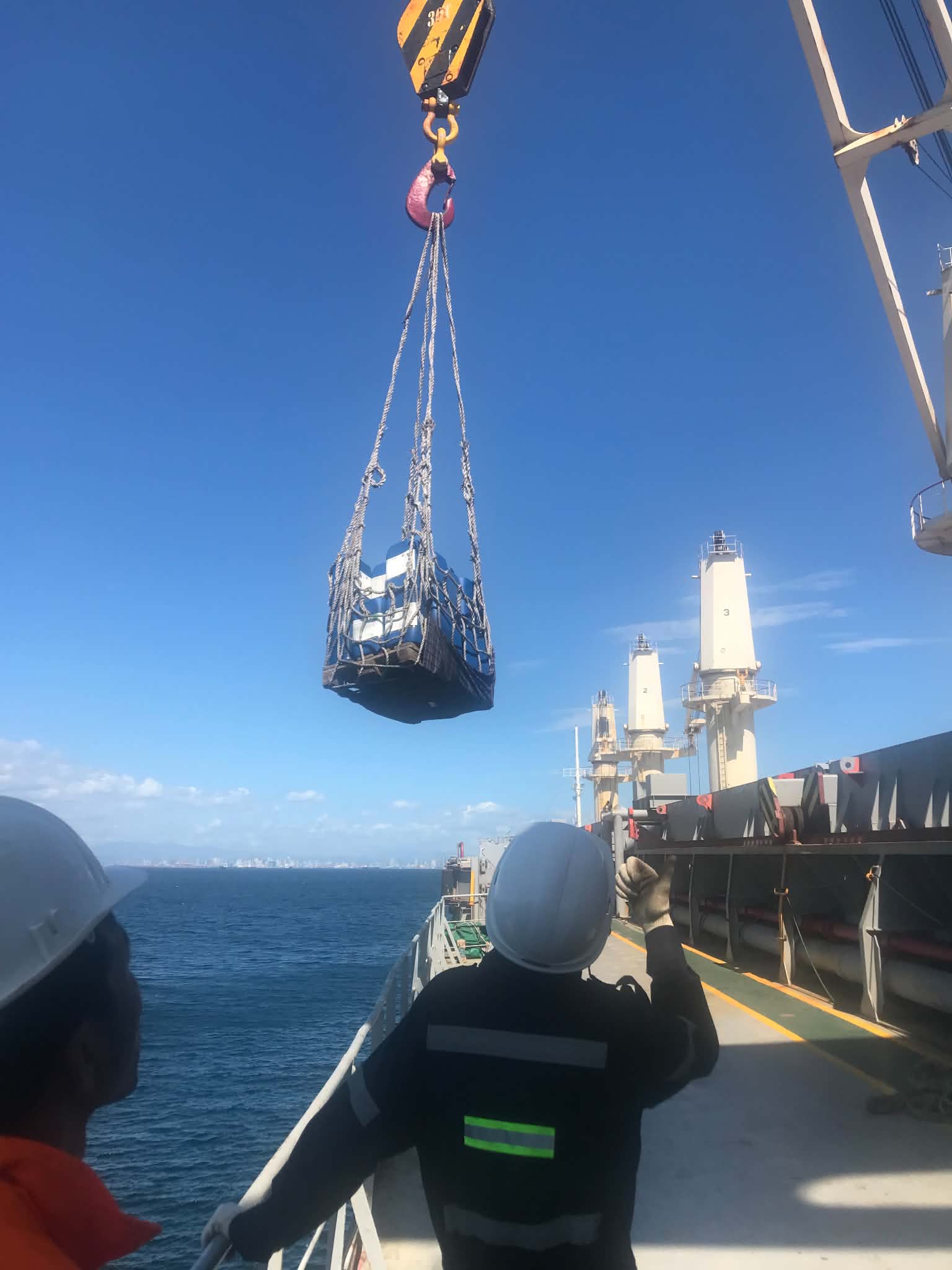 Crane lifting a cargo net of chemical drums from a delivery boat